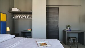 Habitación de hotel con cama, escritorio, silla, armario y estante con toallas y una planta.