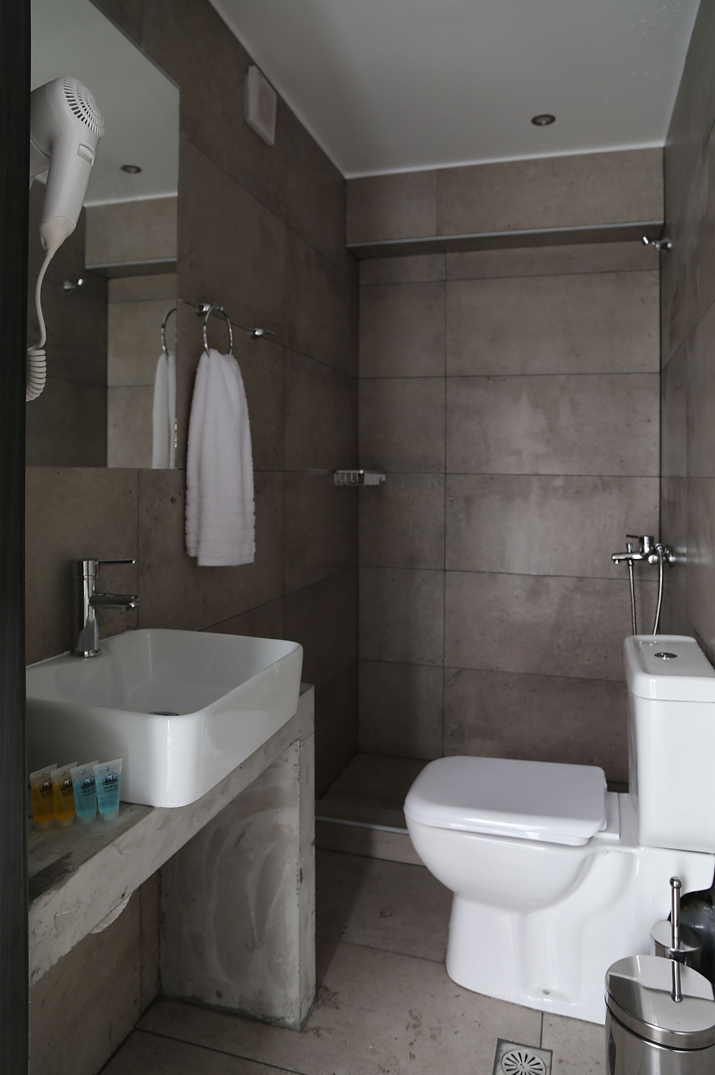 A modern bathroom with a sink, mirror, towel rack, shower, and toilet.