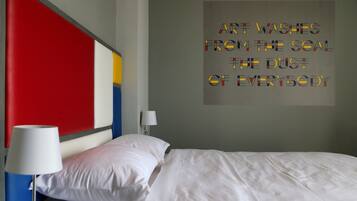 A modern hotel room with a large bed, white bedding, a red accent wall, and a motivational quote on the wall.