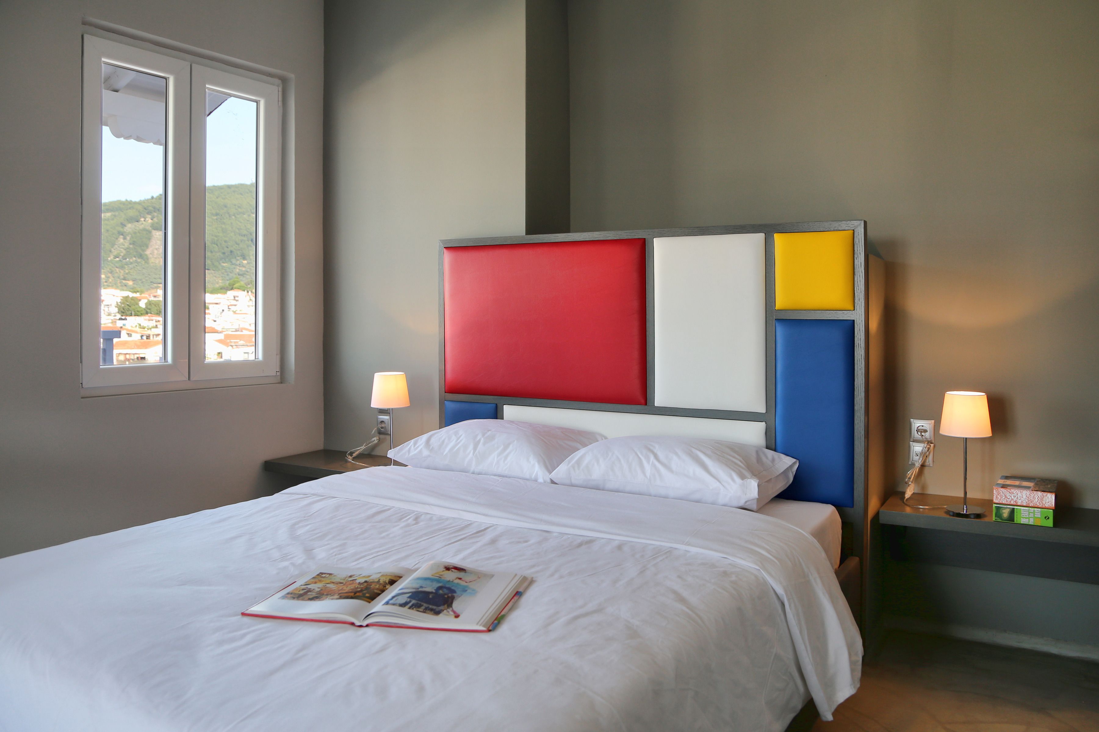 A neatly made bed with white bedding, a red and blue headboard, and a book on the bed.