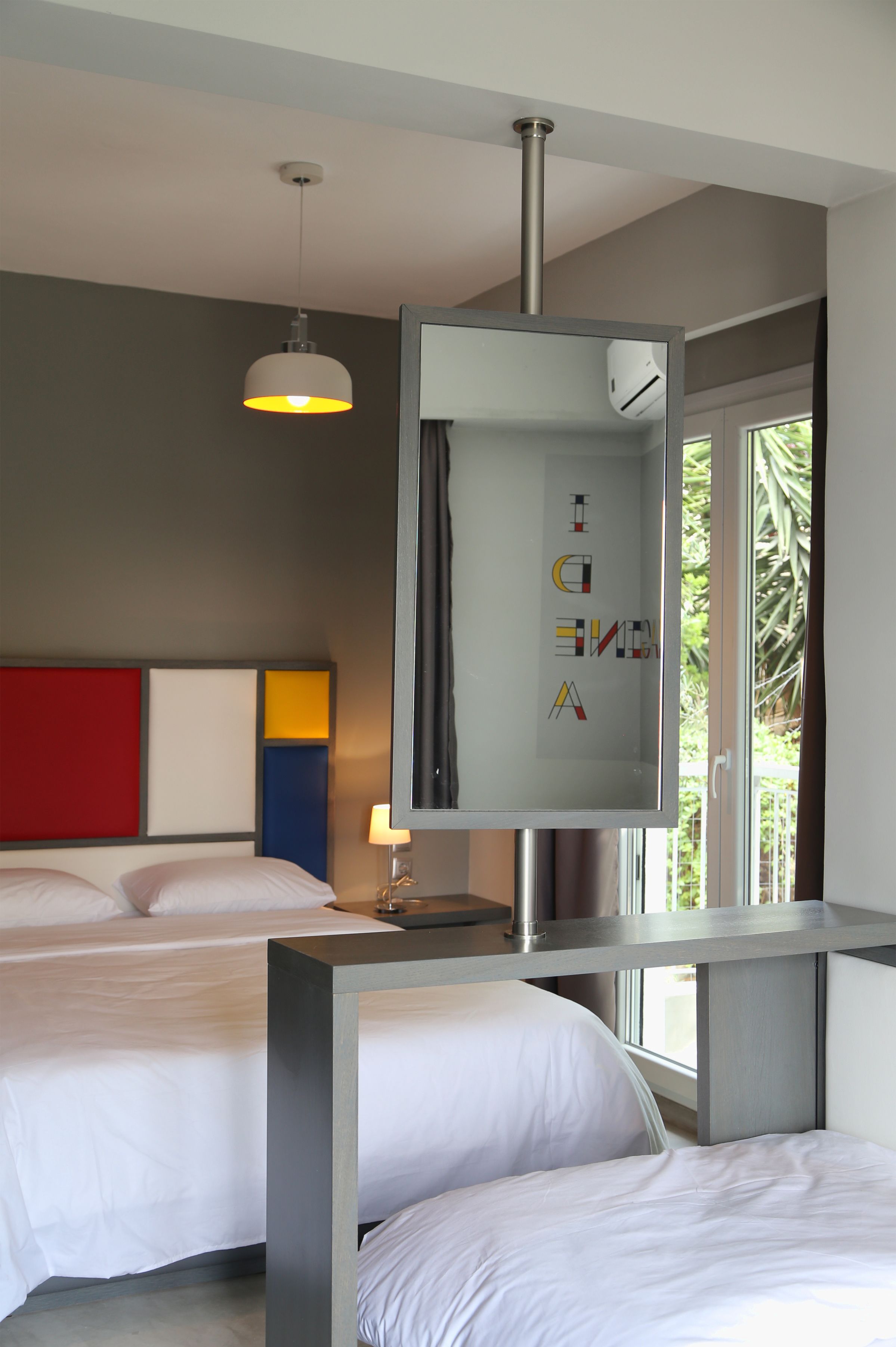 Una habitación de hotel moderna con dos camas, un espejo grande y un ventanal con vistas a zonas verdes.