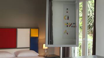 A modern hotel room with two beds, a large mirror, and a window with a view of greenery.