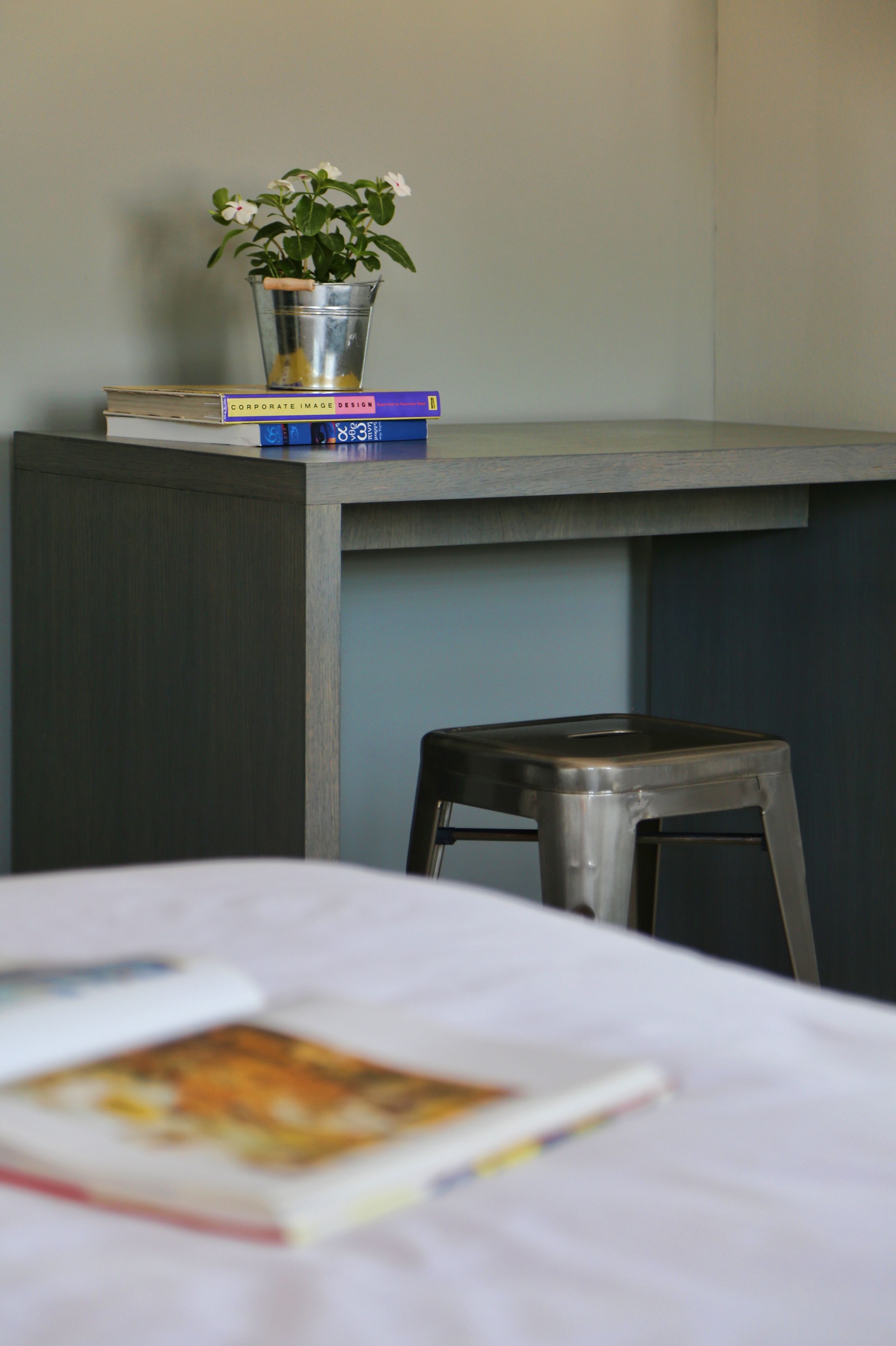 A desk with a metal bucket containing a plant, a stack of books, and a stool.