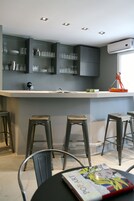 Una cocina moderna con gabinetes grises, una encimera blanca y una barra con taburetes.