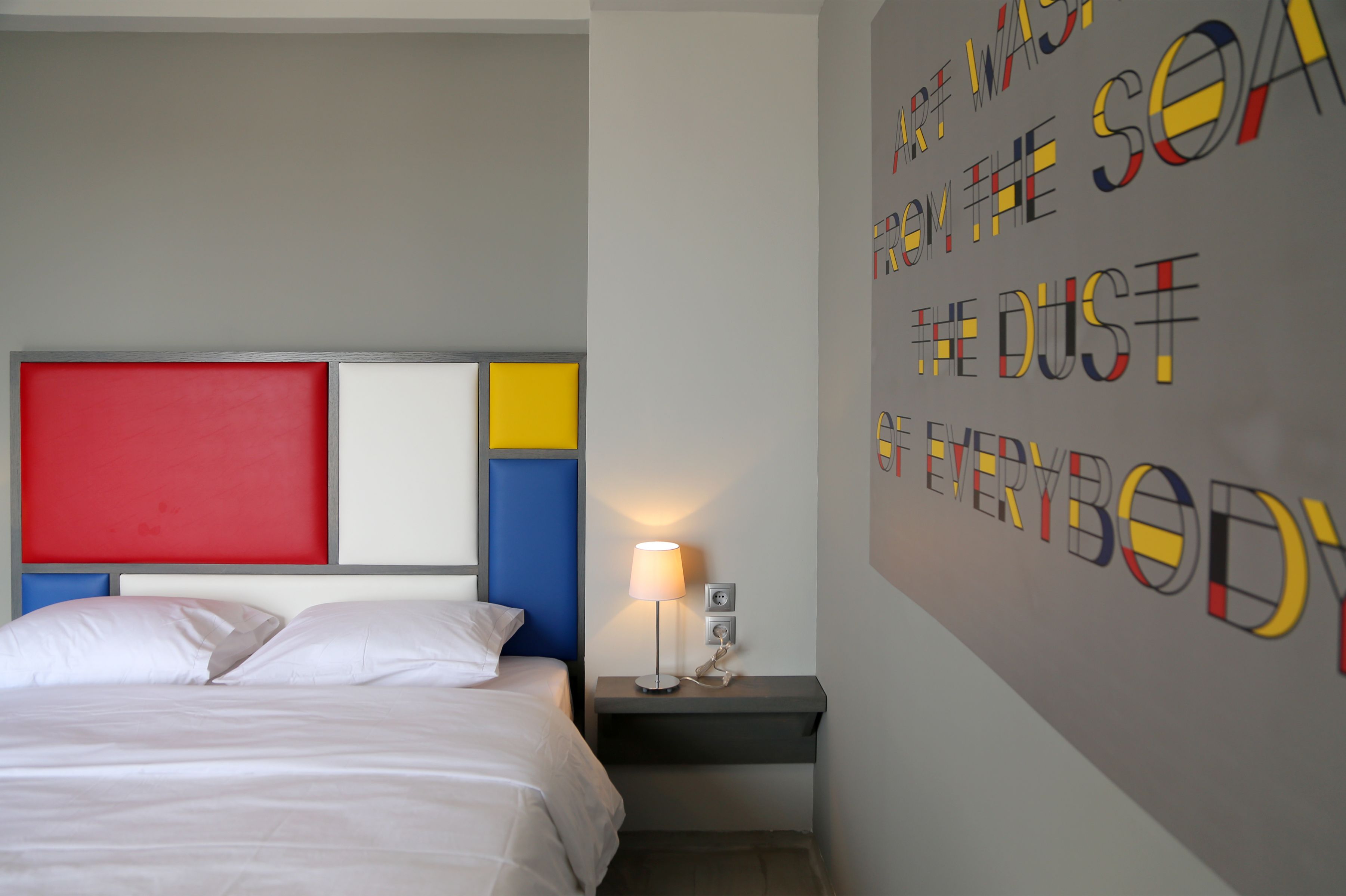 Una habitación de hotel con una cama, una mesita de noche y una pared con texto colorido.
