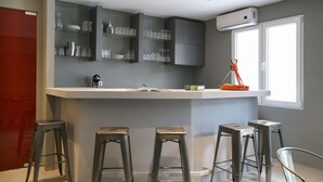 Una cocina moderna con gabinetes grises, una encimera blanca y cuatro taburetes de metal.