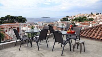 A terrace with outdoor seating, a view of the sea, and a cityscape in the background.