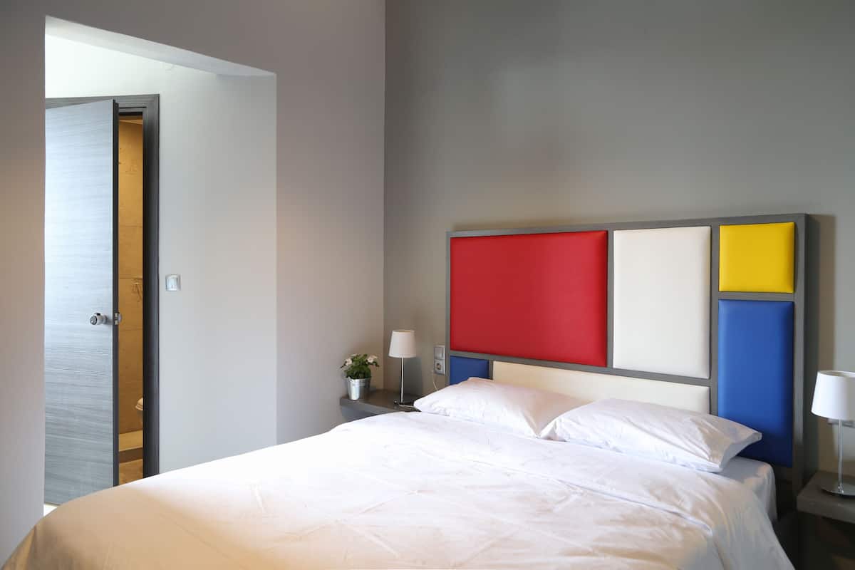 A hotel room with a bed, a nightstand, a lamp, and a wall with a colorful panel.