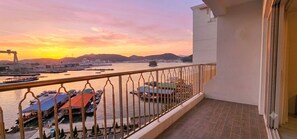 A balcony with a view of a marina and boats, a clear sky, and distant mountains.