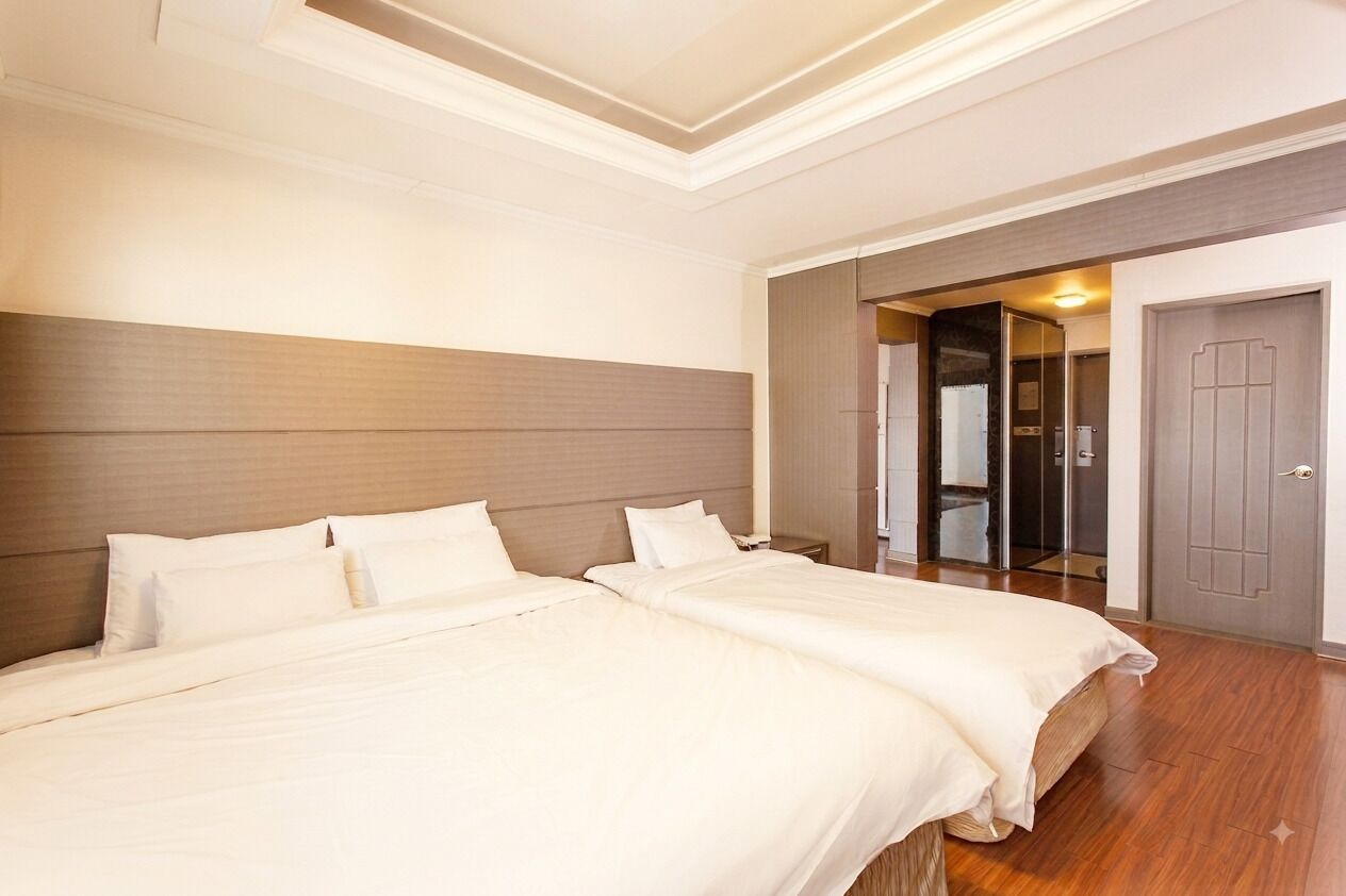 A hotel room with two beds, a wooden headboard, a wardrobe, and a door leading to a bathroom.