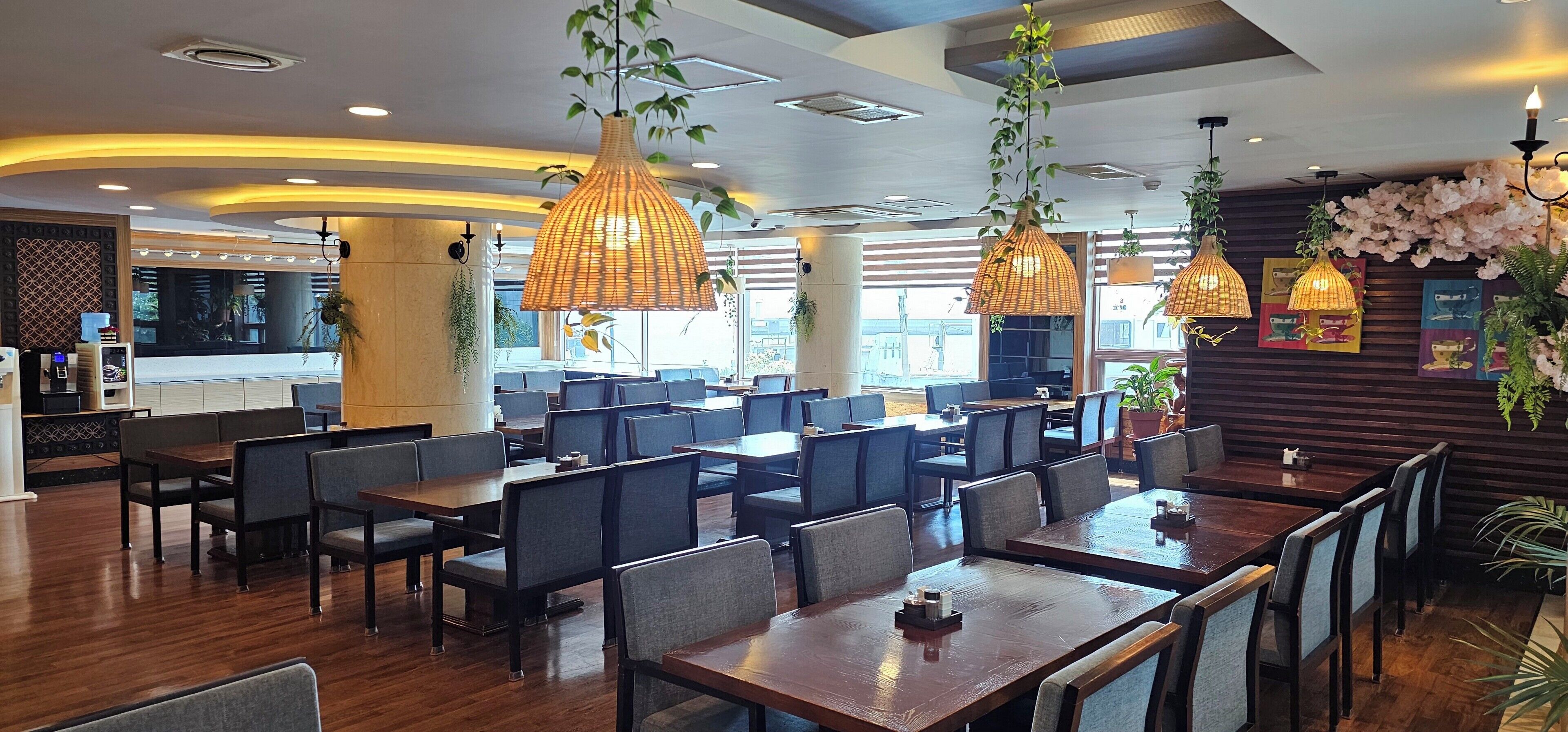 A restaurant with wooden tables and chairs, hanging wicker lamps, and a wall decorated with flowers and artwork.