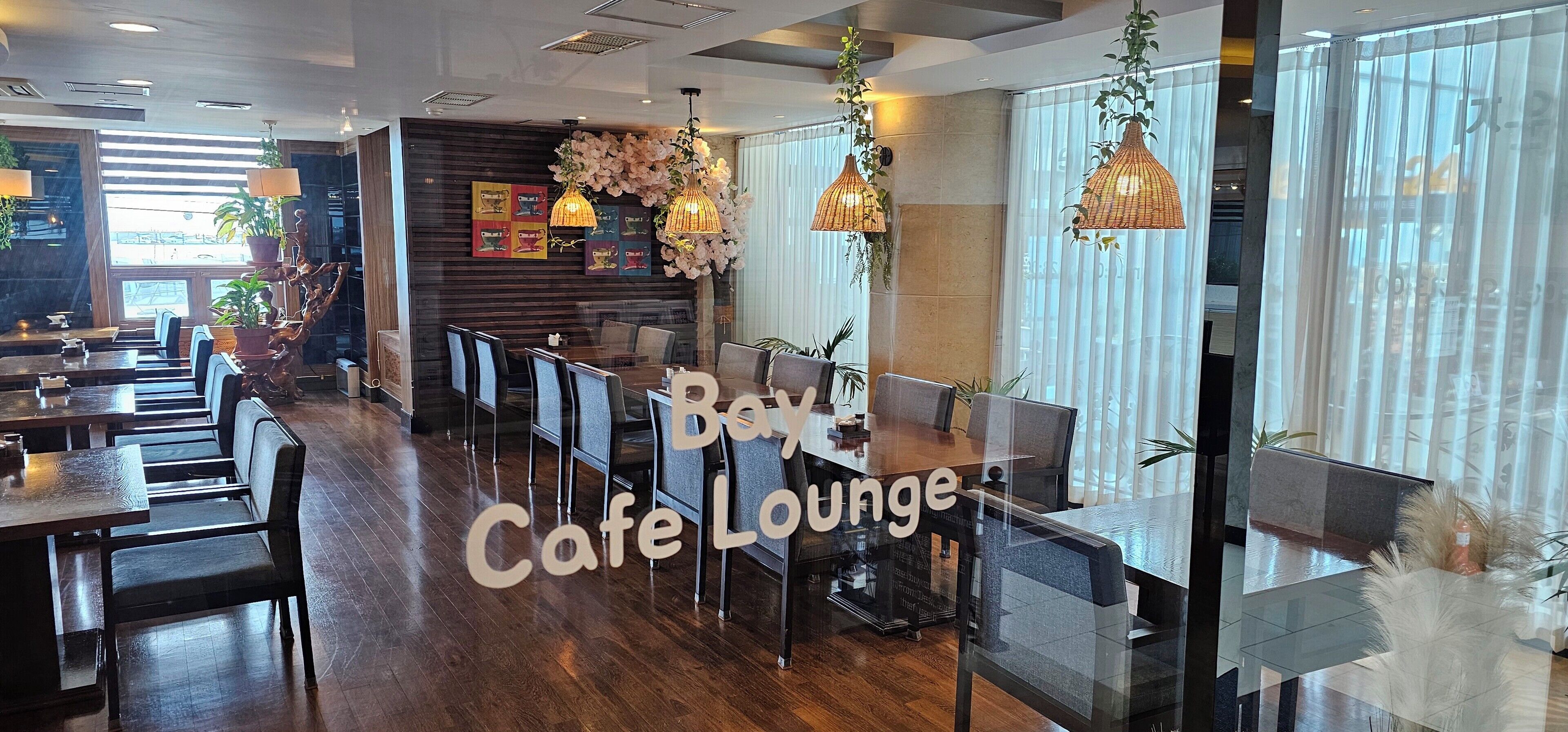 Un salón de café con suelo de madera, separadores de vidrio y lámparas colgantes de mimbre.