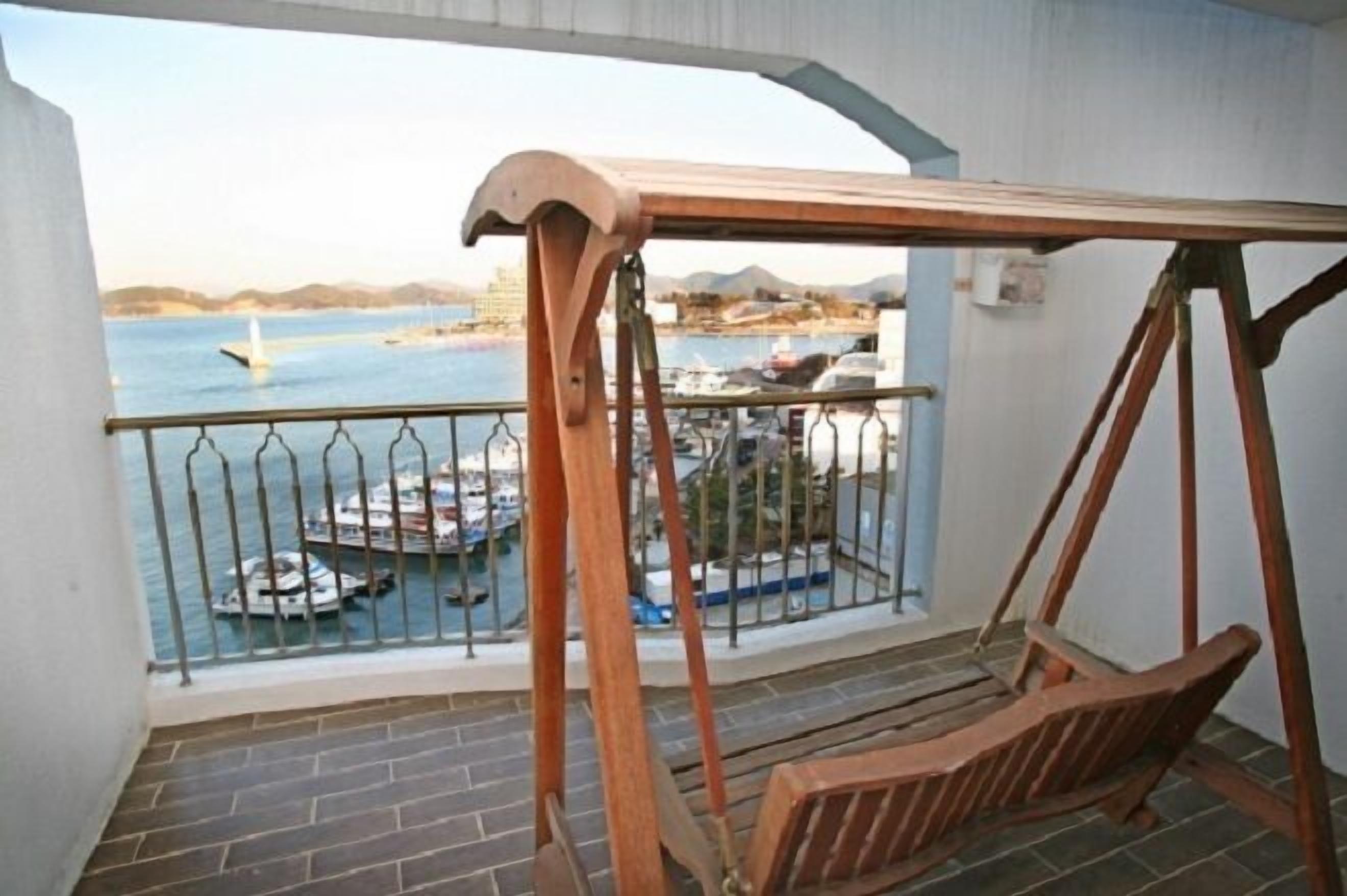 A balcony with a wooden swing and a view of boats and a marina.