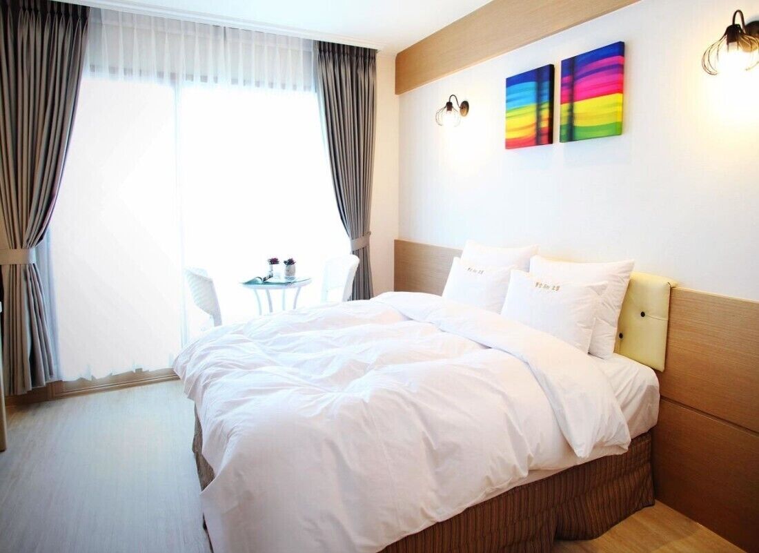 Habitación de hotel con una cama grande, una mesita pequeña y dos lámparas de pared.
