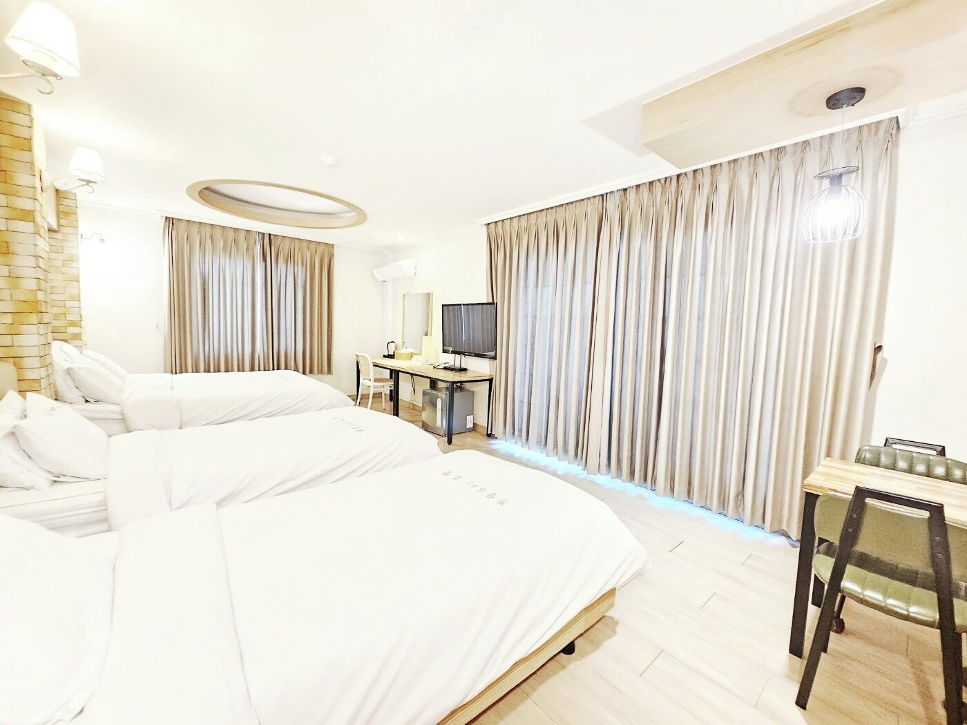 A hotel room with two beds, a desk, a chair, a TV, and curtains.