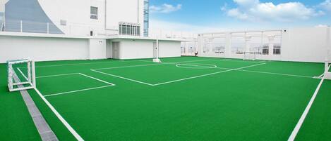 Una cancha deportiva en la azotea, con un portero, rodeada de paredes blancas y amplios ventanales.