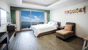 A hotel room with a large bed, a desk, a chair, and a view of the sea.