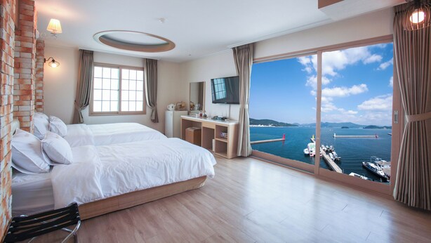 A hotel room with a large bed, a desk, a TV, and a view of the sea.