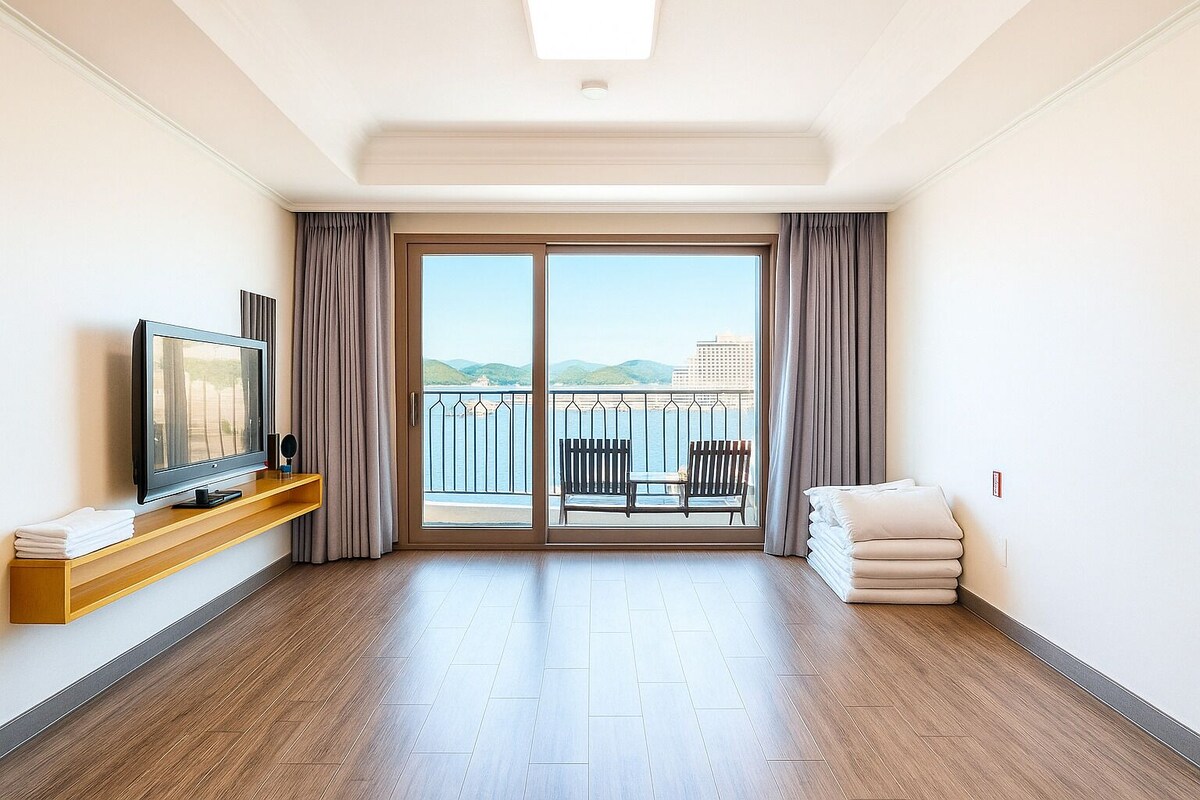 A hotel room with a TV, a wooden shelf, a balcony with chairs, and a bed.