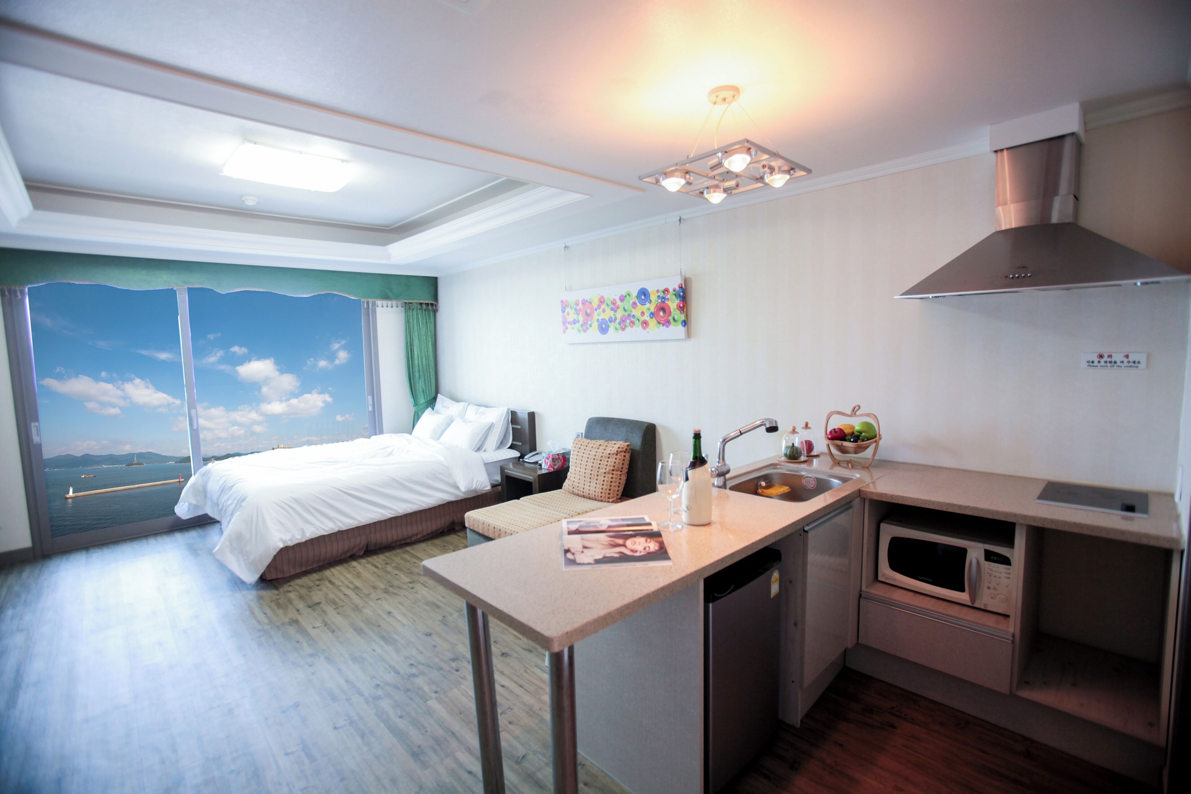 Una habitación de hotel con cama, una kitchenette pequeña, una ventana con vista al mar y un cuadro en la pared.