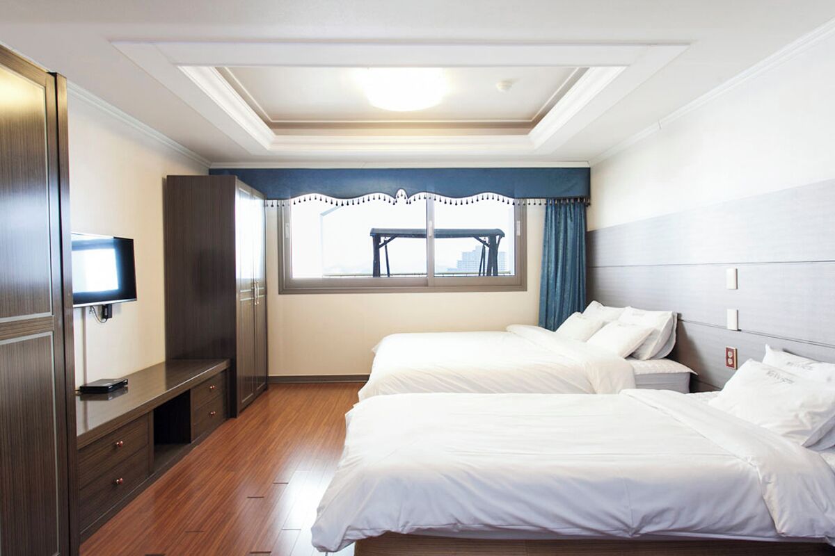 A hotel room with two beds, a TV, a wardrobe, and a window with a view of a cityscape.
