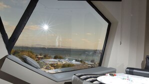 Una habitación moderna con un amplio ventanal que ofrece vistas a un horizonte urbano y una masa de agua.