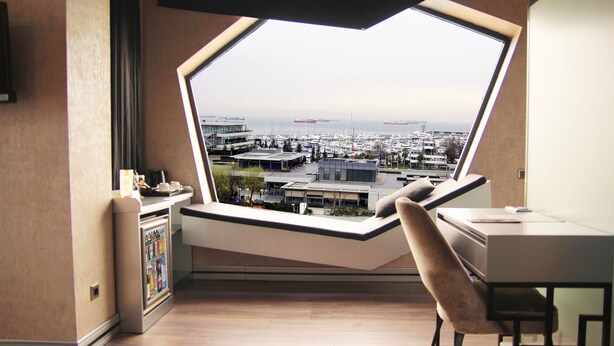 Habitación con un amplio ventanal que da a un puerto deportivo y al paisaje urbano.