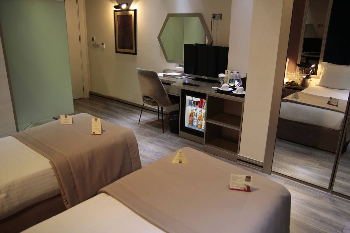 A hotel room with two beds, a desk with a computer, a refrigerator, and a mirror.