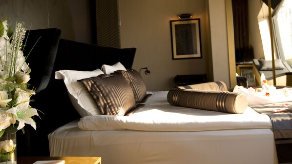 A neatly made bed with white linens and multiple pillows, a vase with white flowers, and a framed picture on the wall.