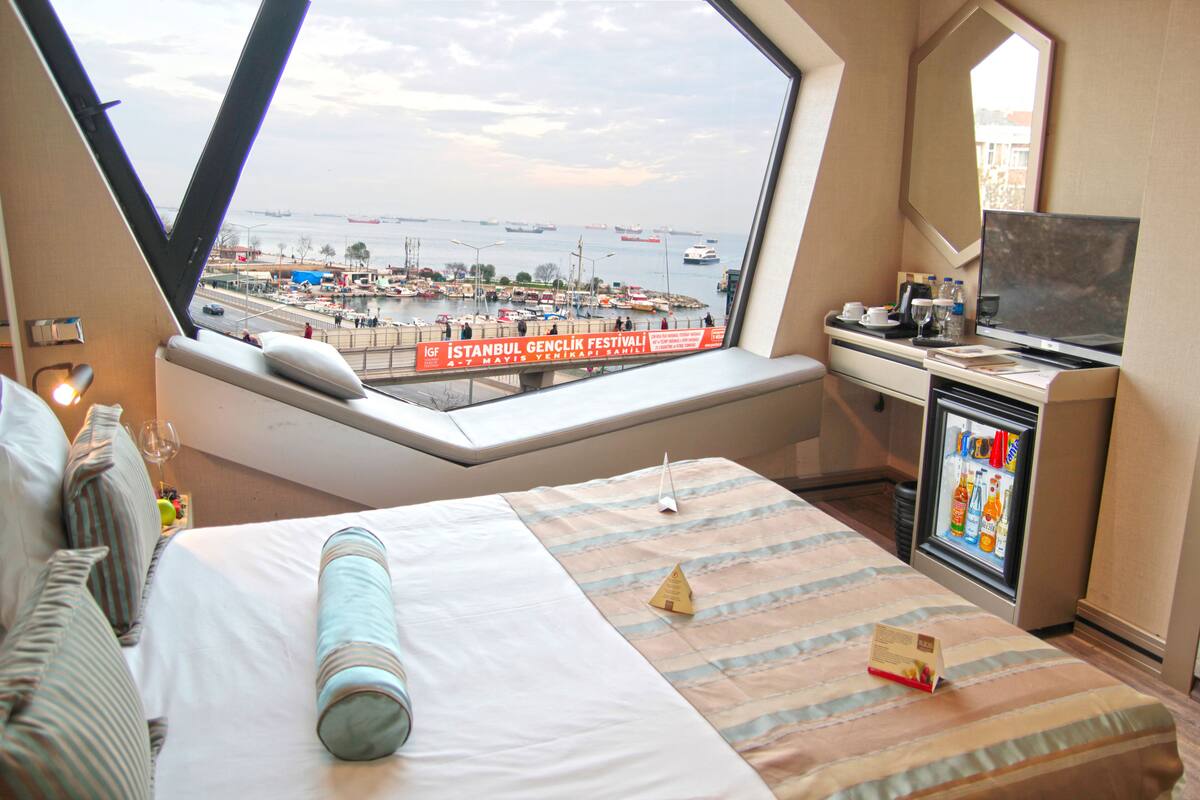 A hotel room with a large window offering a view of a harbor and a festival banner.