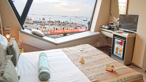 Habitación de hotel con un ventanal amplio que ofrece vistas a un puerto y un cartel de festival.