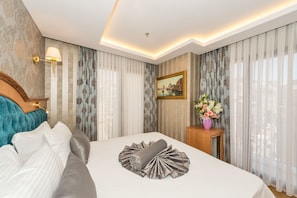 A hotel room with a neatly made bed, a wooden headboard, a nightstand with a vase of flowers, and a painting on the wall. - Aprilis Gold Hotel - Special Class (Istanbul)
