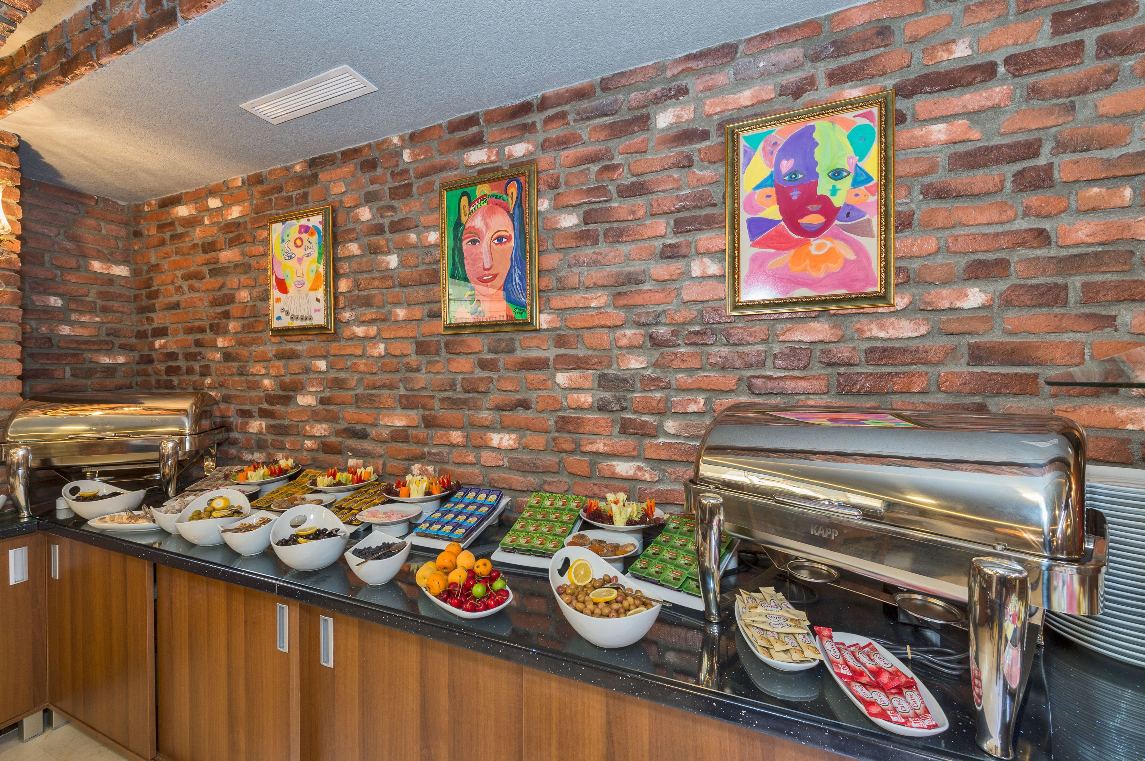 A buffet setup with various food items and a brick wall with framed artwork.