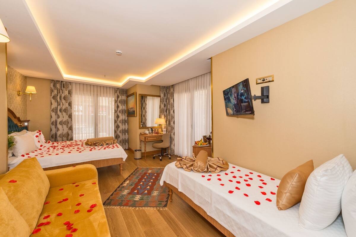 A hotel room with two beds, a desk, a sofa, and a TV.