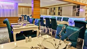 A restaurant with teal chairs, white tables, and a bar area with shelves of bottles. - Rota Bulvar Hotel (Ankara)