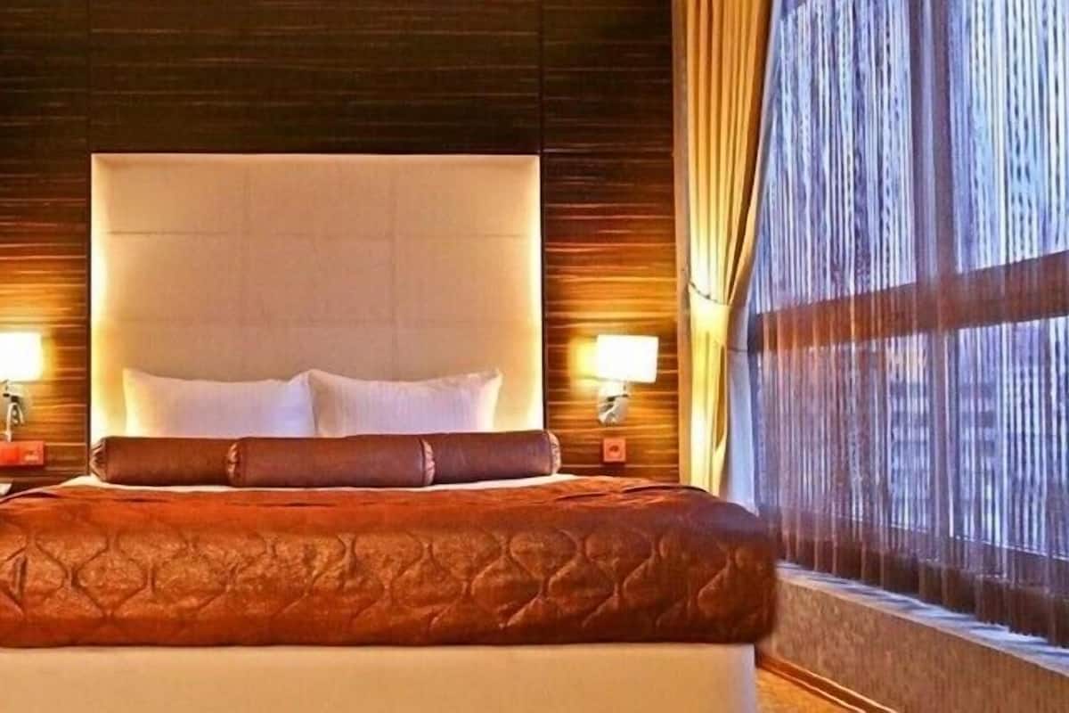 Una habitació d'hotel amb un llit gran, panells de fusta a les parets, dues làmpades de nit i una finestra amb cortines.