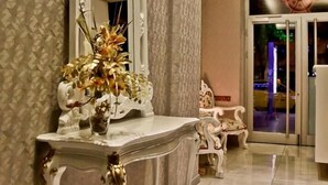 A hallway with a large ornate mirror, a white console table with a vase of flowers, and a patterned wall. - Rota Bulvar Hotel (Ankara)