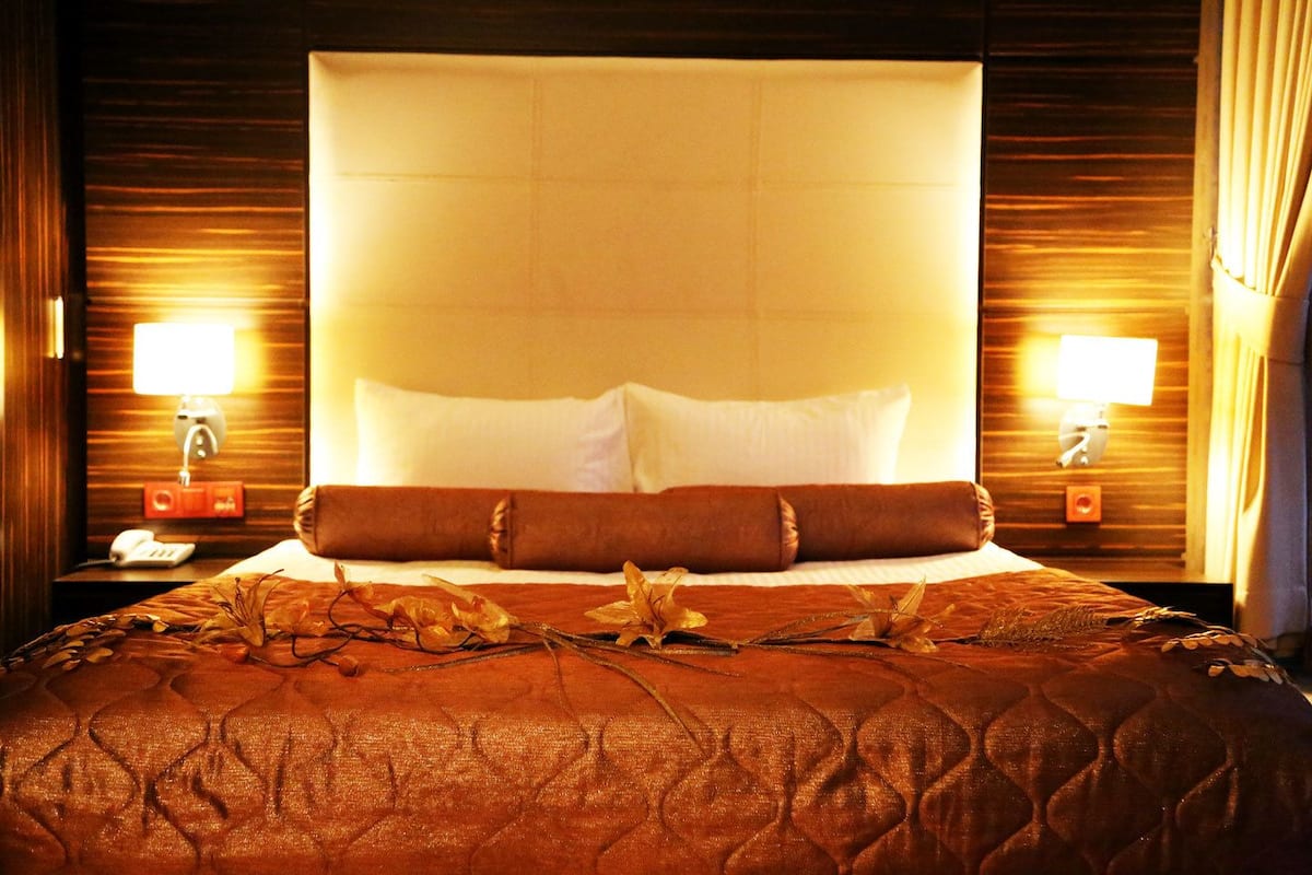 Habitació d'hotel amb un llit gran, dues làmpades laterals i un panell de llit de fusta.