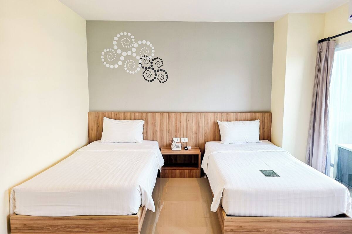 A hotel room with two single beds, a wooden headboard, a nightstand with a phone, and a wall art piece.