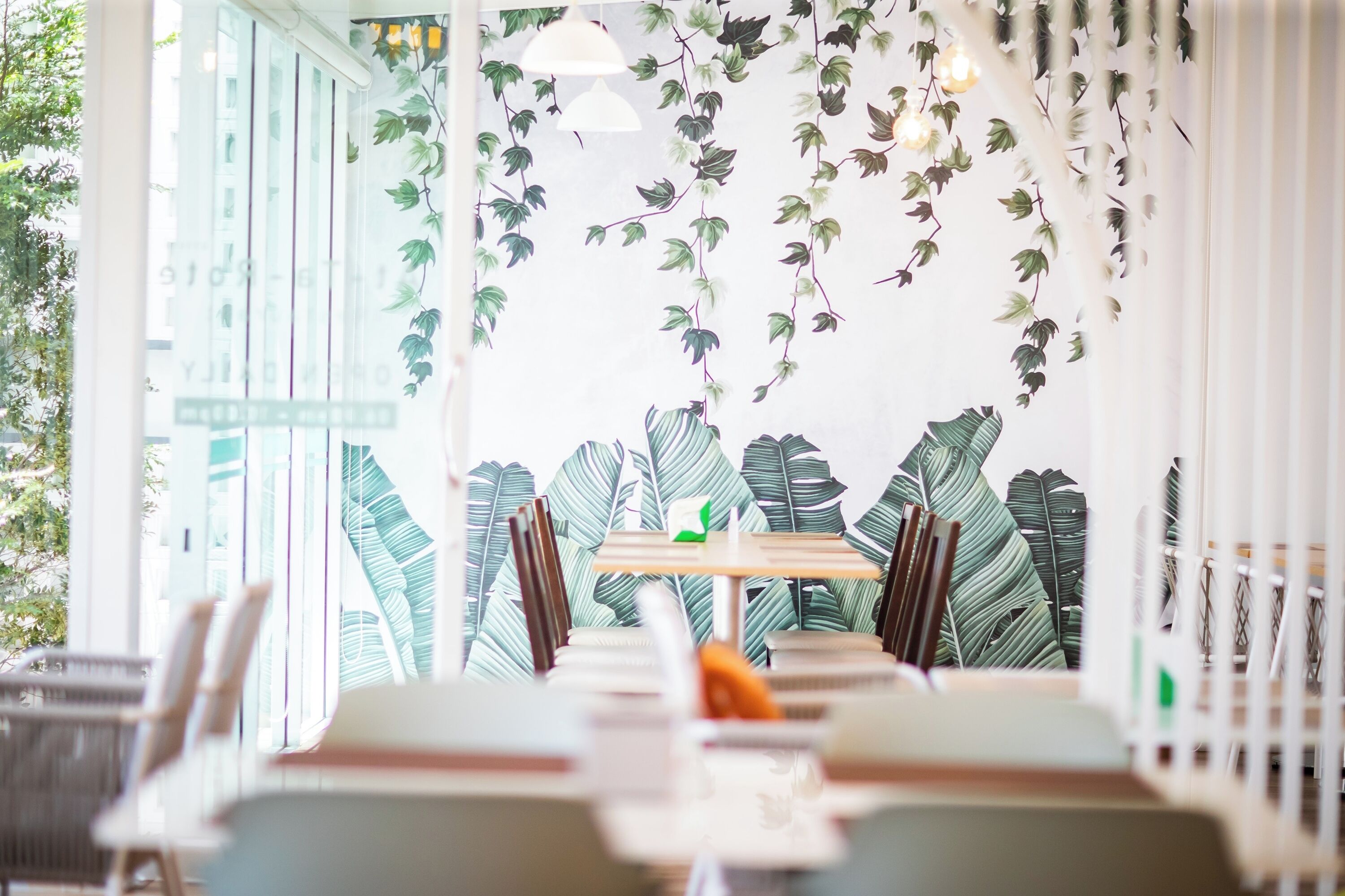 A restaurant with a modern interior, featuring a table with chairs, a hanging light fixture, and a wall decorated with leafy patterns.