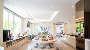 Un moderno vestíbulo de hotel con una barra de desayuno circular central, zonas de estar y grandes ventanales con vistas a zonas verdes.