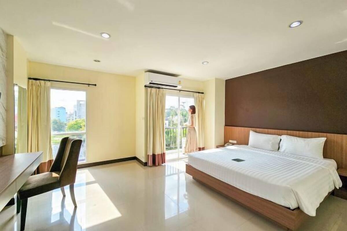 A hotel room with a bed, a desk, a chair, and a balcony with curtains.