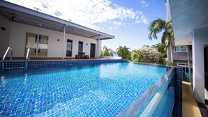 Un área de piscina moderna con una piscina azul cristalina, un deck cubierto y un edificio con ventanas amplias y techo plano.