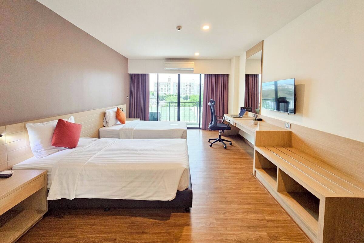 A hotel room with two beds, a desk, a chair, a TV, and a large window.