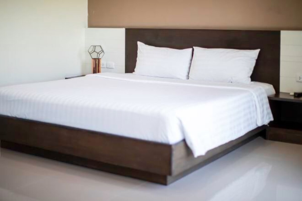 A large bed with a wooden headboard, white bedding, and a bedside table with a lamp.