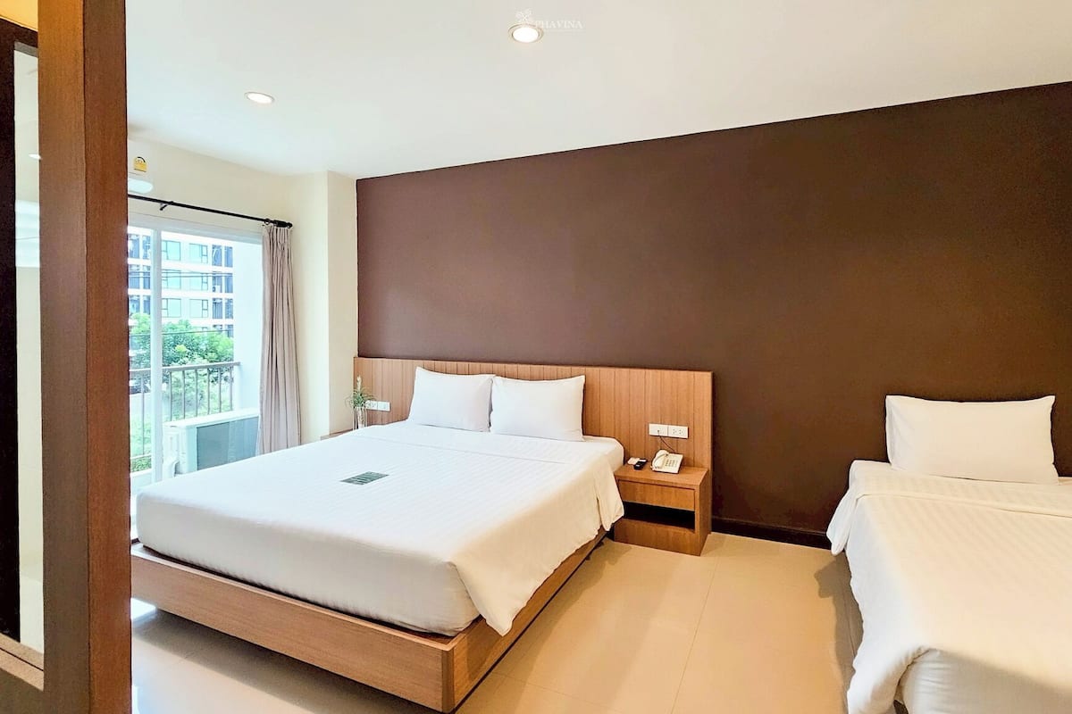 A hotel room with a large bed, a smaller bed, a bedside table with a phone, and a window with a view of buildings.
