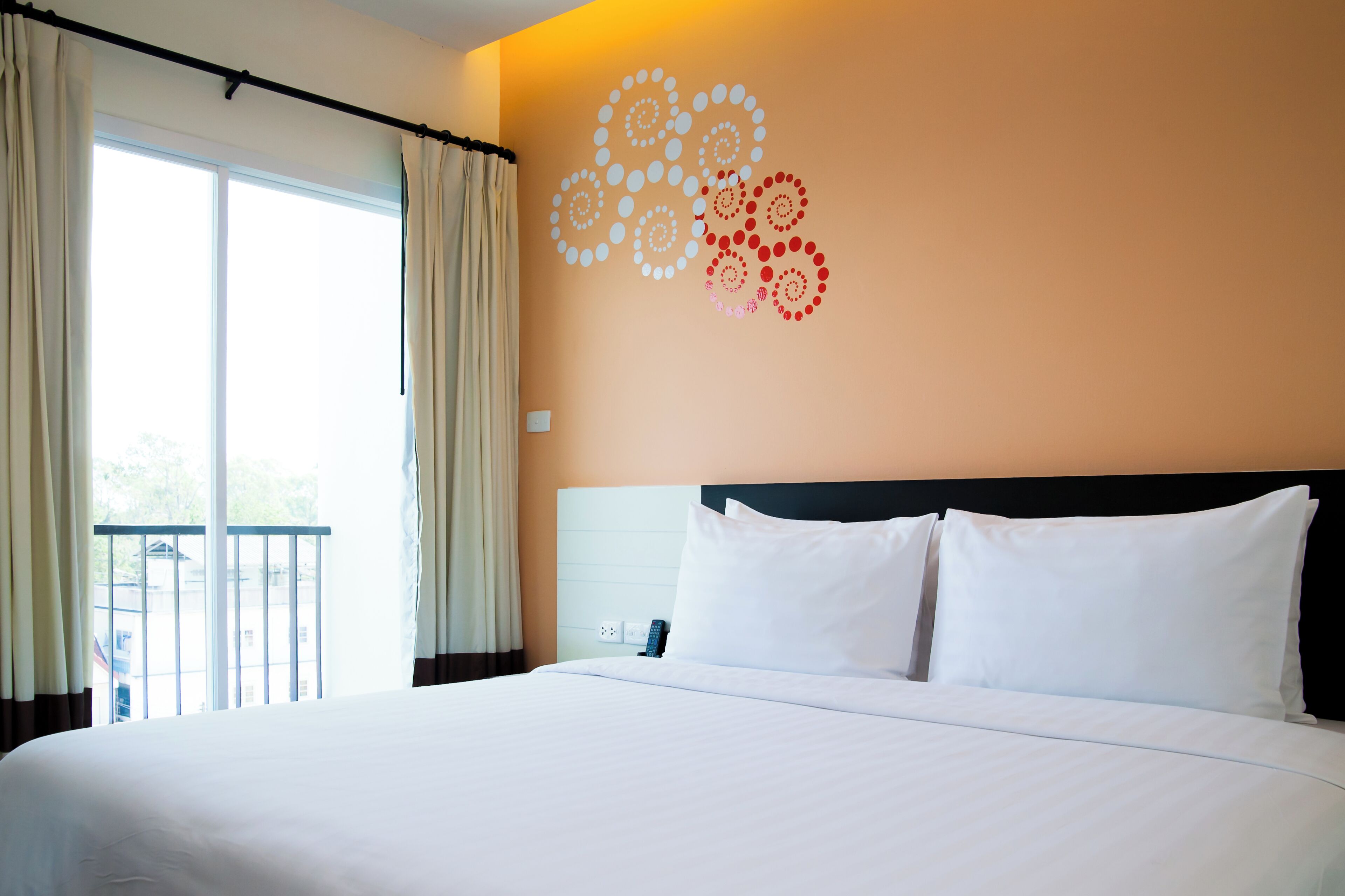 A hotel room with a large bed, a view of the outdoors, and a wall with circular patterns.