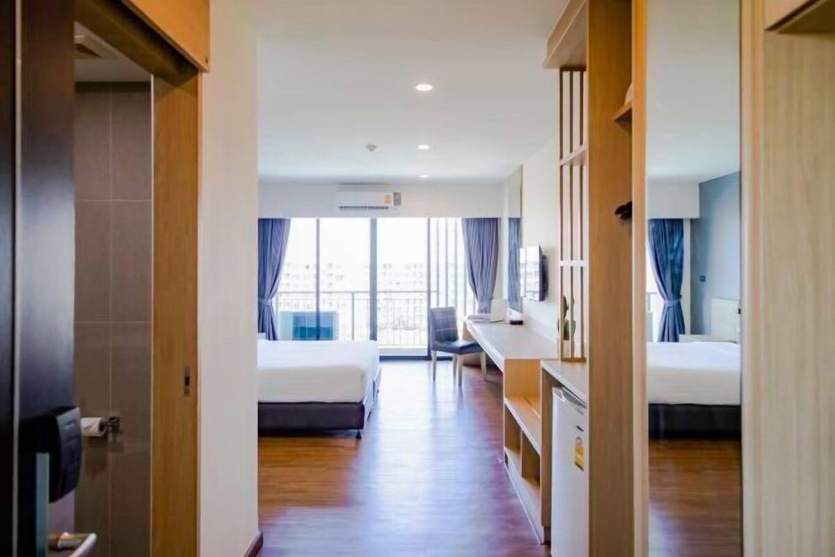 A hotel room with a bed, a desk, and a chair. There is a window with curtains and a view of buildings outside.