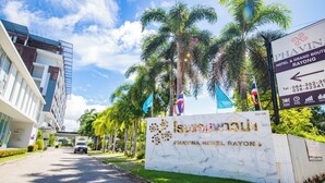 Entrada de un hotel con un cartel que dice 'Phavina Hotel Rayong' y una calle bordeada de palmeras.
