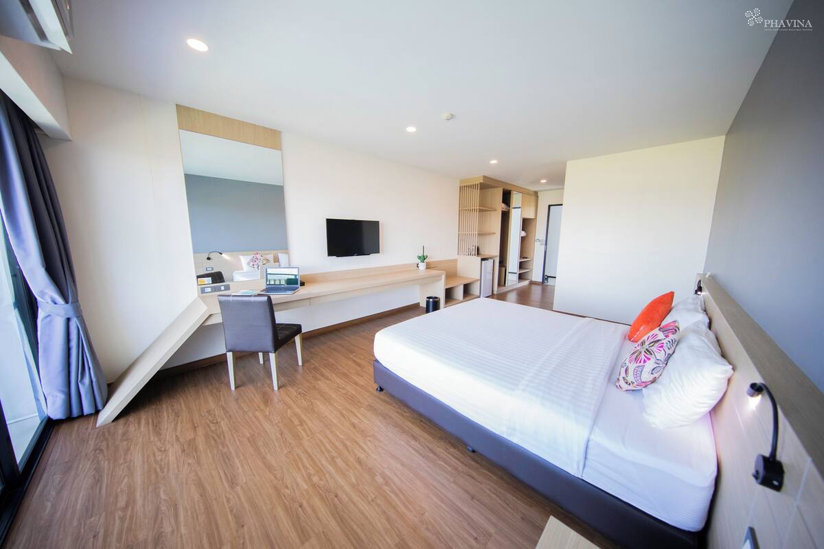 A modern hotel room with a bed, desk, chair, and a TV mounted on the wall.